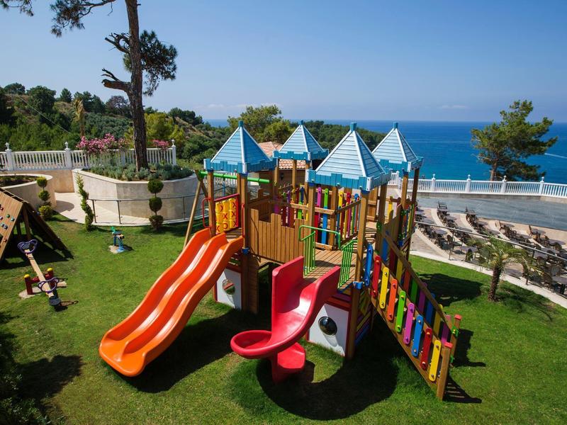 Colorful playground with slides and climbing structures on grass overlooking the sea.