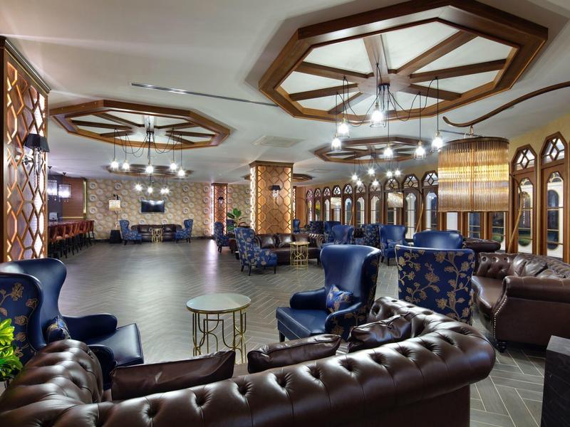Spacious hotel lounge with brown leather sofas, blue armchairs, and decorative ceiling lights.