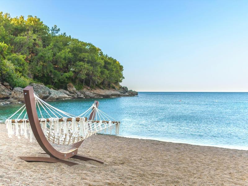 Hammock on sandy beach overlooking the sea with wooded hill in the background