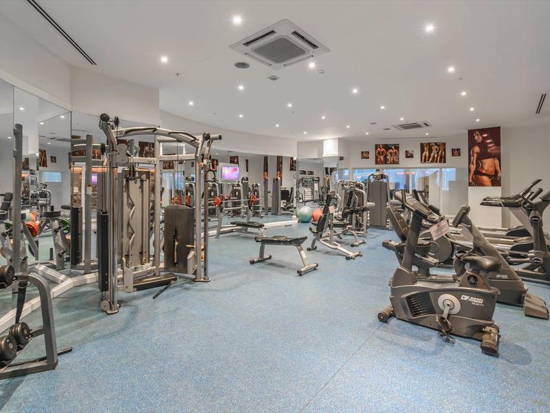 Modern gym room with various exercise machines and bright blue carpet flooring.