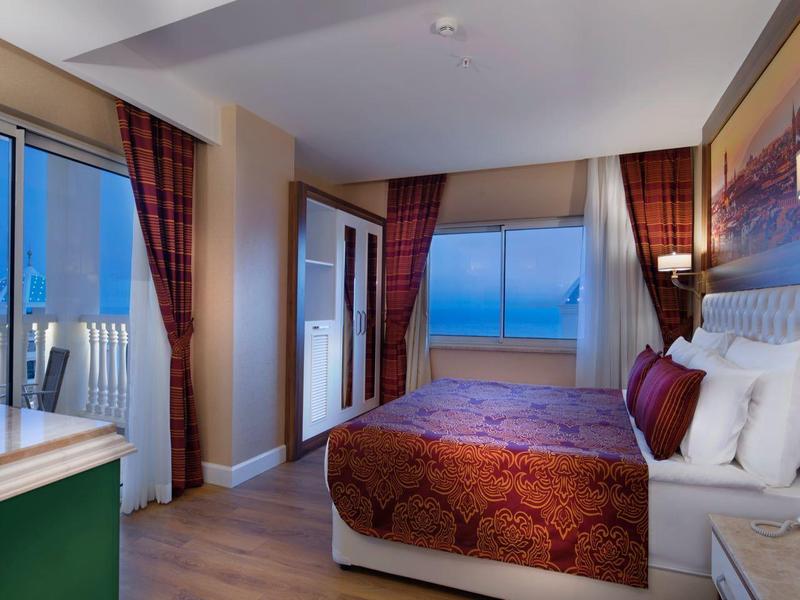 Elegant hotel room with king-size bed, balcony, and sea view at sunset.