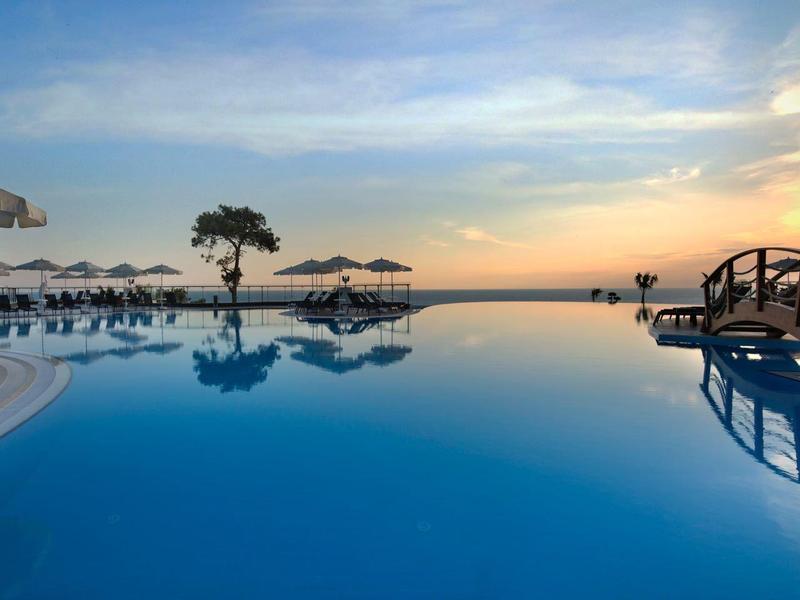 Infinity pool with sun loungers and sunset view over the sea.
