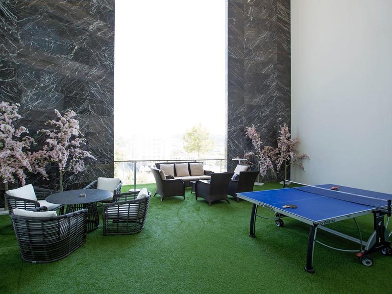Modern lounge area with green carpet, ping pong table, and seating by large windows