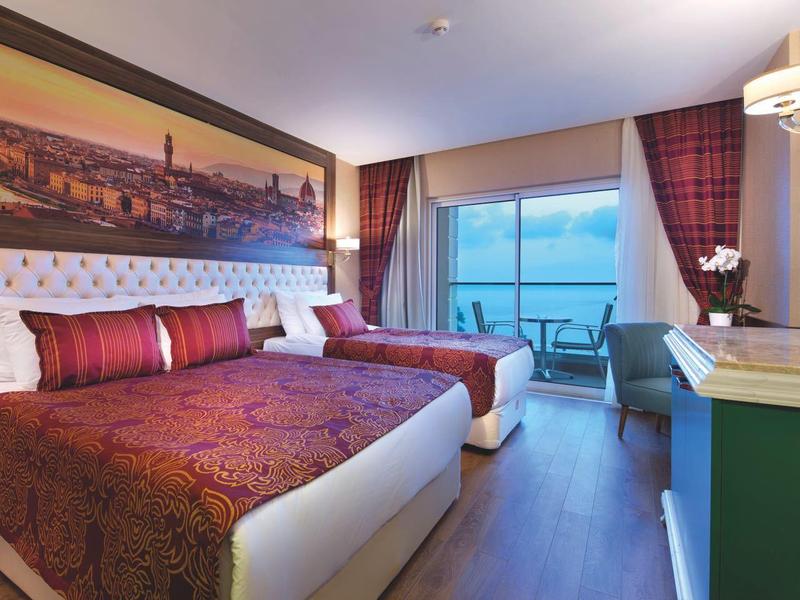 Modern bedroom with large bed, balcony view, and elegant decor in warm tones.