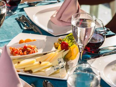 Elegantes Tischgedeck mit weißem Geschirr, Wein und Wasser, Käseplatte und Servietten in Pastellfarben.