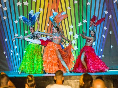 Tre ballerine in abiti colorati davanti a una parete di sfondo arcobaleno con stelle.