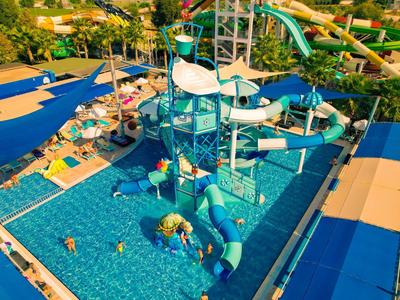 Wasserpark mit blauen Rutschen, Wasserspielen und Schwimmbecken, umgeben von Liegestühlen.