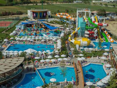 Großer Wasserpark mit mehreren Schwimmbecken, Wasserrutschen, Liegestühlen und grünen Wiesen.