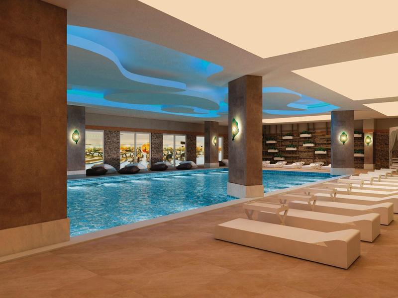 Moderner Innenpool mit blauer Beleuchtung, braunen Säulen und weißen Liegestühlen am Beckenrand.