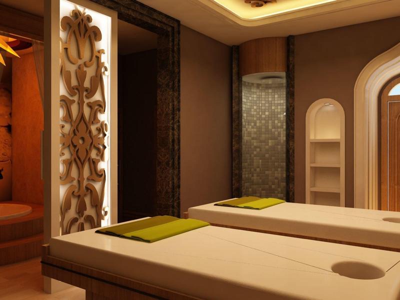 Moderne Wellness-Massageräume mit warmem Licht, zwei Liegen, dekorativen Wandpaneelen und holzfarbener Tür.