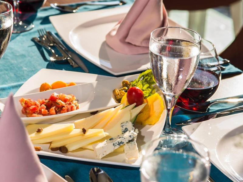 Elegantes Tischgedeck mit weißem Geschirr, Wein und Wasser, Käseplatte und Servietten in Pastellfarben.