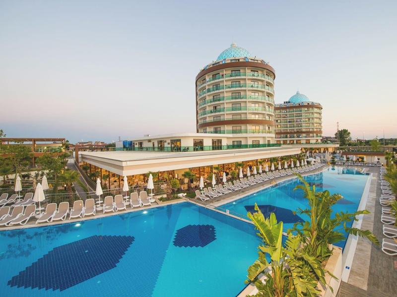 Modernes Hotel mit rundem Turm, großem Pool und zahlreichen Liegestühlen bei klarem Himmel.