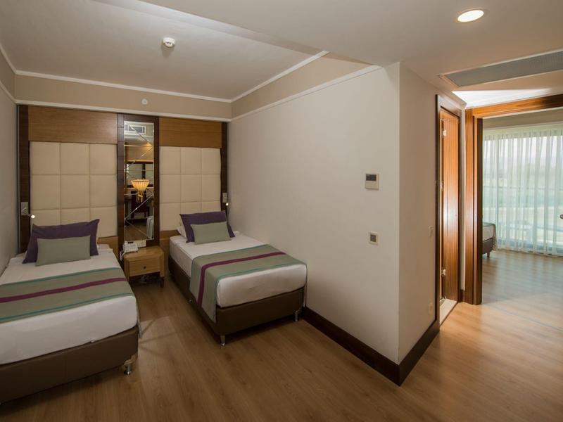 Hotelzimmer mit zwei Einzelbetten, Holzboden, hellen Wänden und Blick auf einen Balkon.