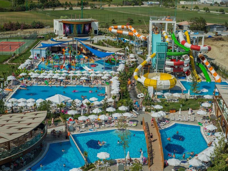 Großer Wasserpark mit mehreren Schwimmbecken, Wasserrutschen, Liegestühlen und grünen Wiesen.