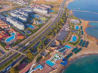 Luftaufnahme eines Küstenresorts mit Poolanlagen, mehreren Gebäuden und einer Küstenstraße.