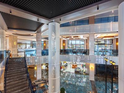 Großer, moderner Hotel-Eingangsbereich mit Glas, Marmorböden, Treppen und gelben Sitzmöbeln.