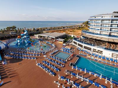 Große Hotelanlage mit mehreren Pools, blauen Liegestühlen und Meerblick unter klarem Himmel.