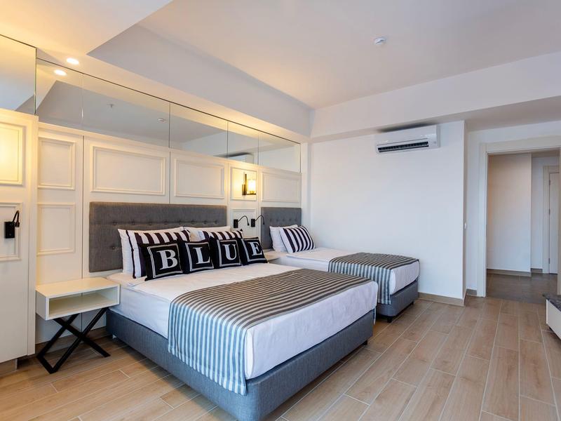 Modernes Schlafzimmer mit grauem Bett, gerahmten Kissen, Holzboden und weißen Wänden.