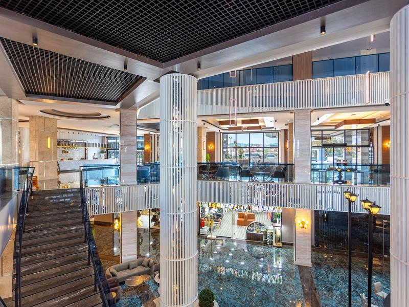 Großer, moderner Hotel-Eingangsbereich mit Glas, Marmorböden, Treppen und gelben Sitzmöbeln.