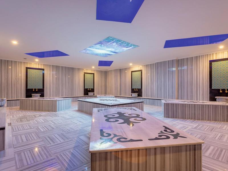 Moderner Spa-Raum mit hellen Fliesen, Kacheln, Wasserbecken und blauen Deckenleuchten.