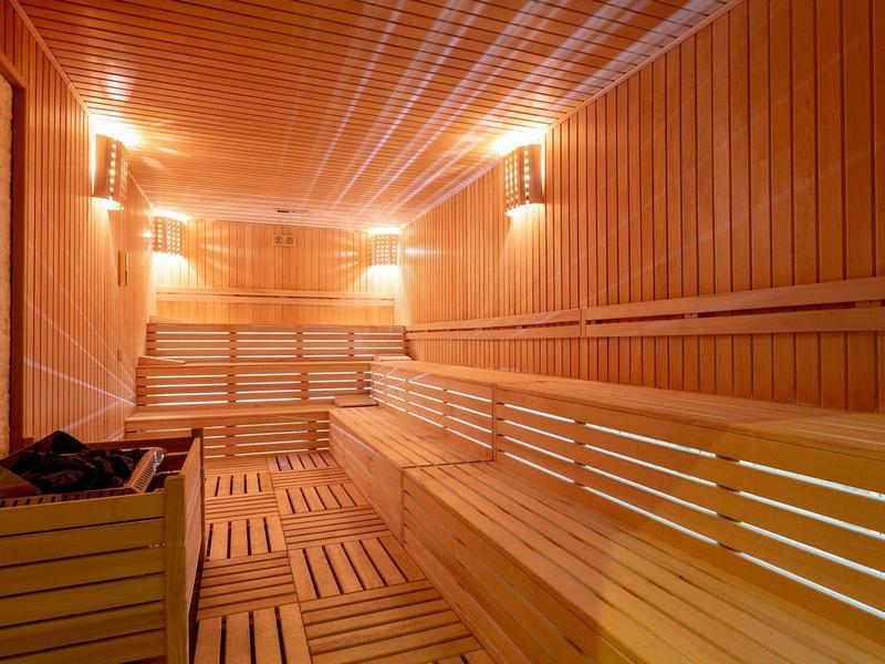 Großer Saunaraum mit Holzverkleidung, mehrstufigen Sitzbänken und warmem Licht.