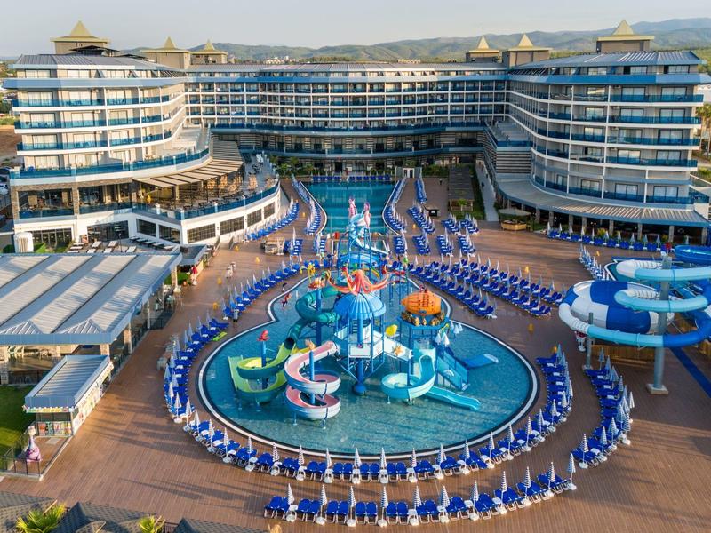 Großes Hotel mit blau-weißen Liegestühlen rund um bunte Wasserrutschen und Kinderpool.