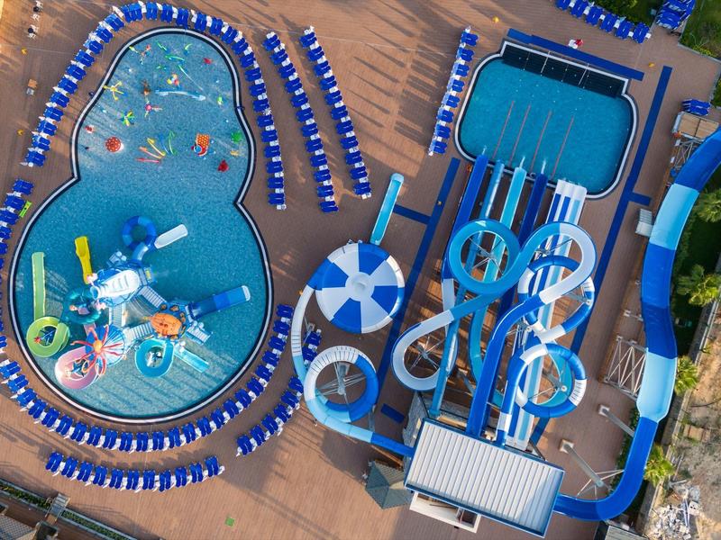 Luftaufnahme eines großen Wasserparks mit Schwimmbecken, Wasserrutschen und Sonnenliegen.