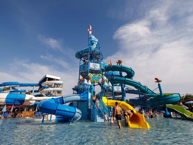 Wasserpark mit bunten Rutschen, vielen Röhren und einem großen Pool unter blauem Himmel.
