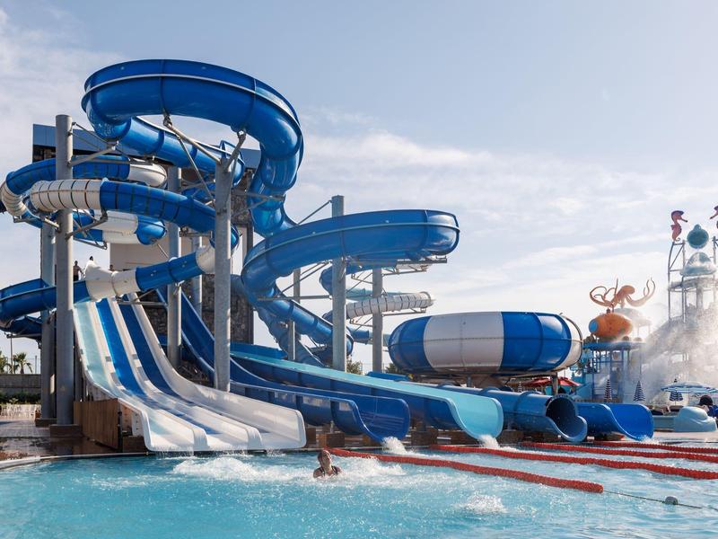 Große blaue Wasserrutschen mit Spiralen und geraden Bahnen in einem Freizeitpark bei klarem Himmel.