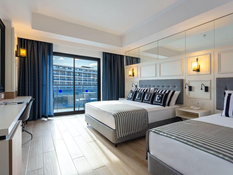 Modernes Hotelzimmer mit zwei Betten, großem Fenster, Holzboden und minimalistischer Einrichtung.