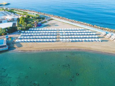 Pláž s uspořádanými lehátky a slunečníky u průzračného moře poblíž hotelového komplexu.