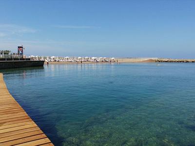 Čistý oceán s dřevěným molem a městem na obzoru za slunečného počasí.