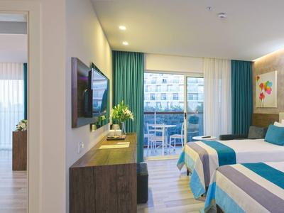 Hotelzimmer mit zwei Betten, modernem Mobiliar, großem Fenster und Balkon mit Stadtblick.
