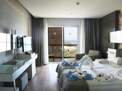 Modernes Hotelzimmer mit Doppelbett, Flachbildfernseher, Glas-Schreibtisch und Meerblick durch Balkon.