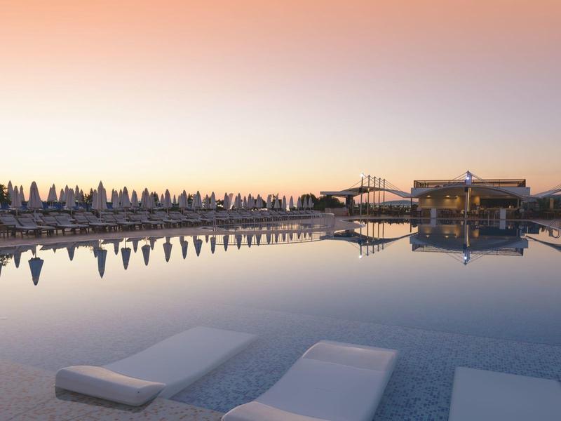 Nekonečný bazén s lehátky při západu slunce v hotelu s výhledem na chatku a most