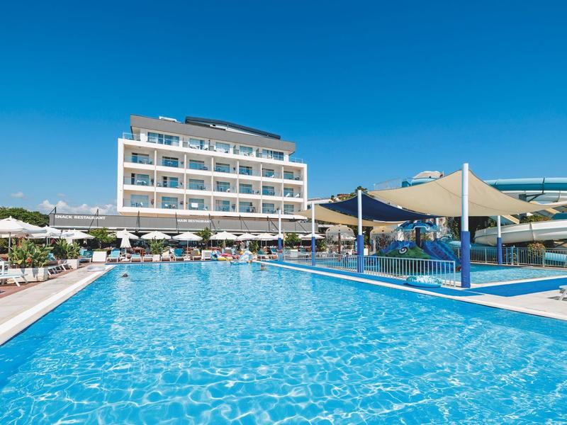 Velký bazén před moderní hotelovou budovou s slunečníky a modrou oblohou.