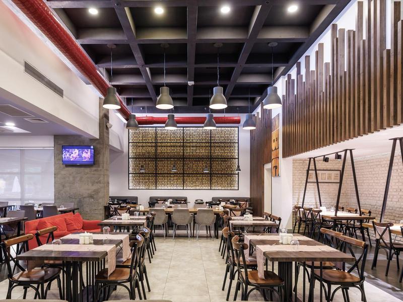 Moderní, prostorná restaurace s dřevěným stropem a mnoha stoly a židlemi pro hosty.