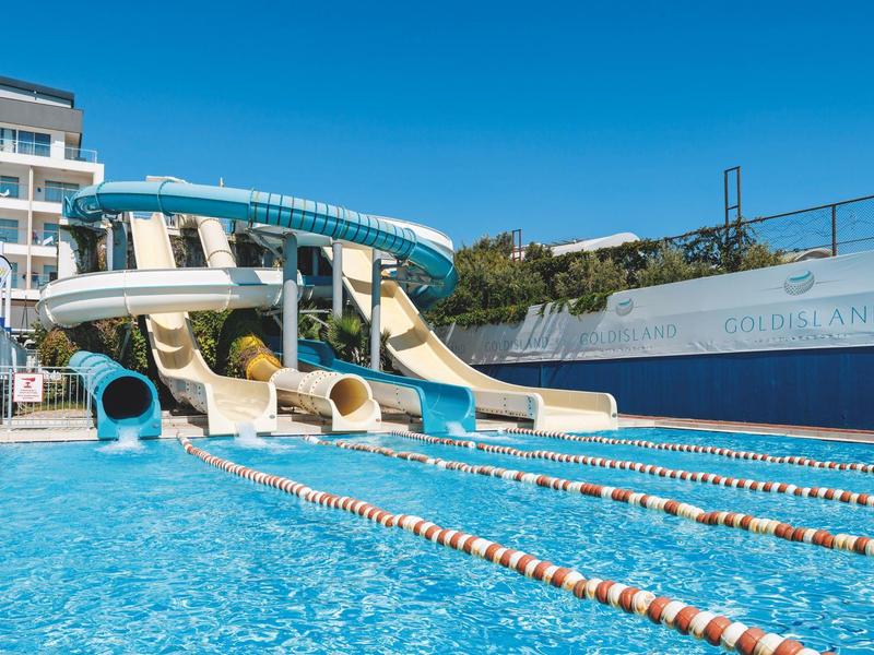 Venkovní bazén s vodními skluzavkami a plaveckými dráhami před hotelem za jasné oblohy.