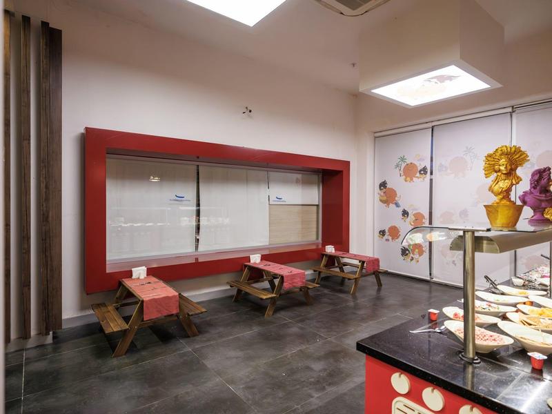 Moderní místnost s červenými lavicemi, tmavou podlahou a dekorativními figurkami na stole.