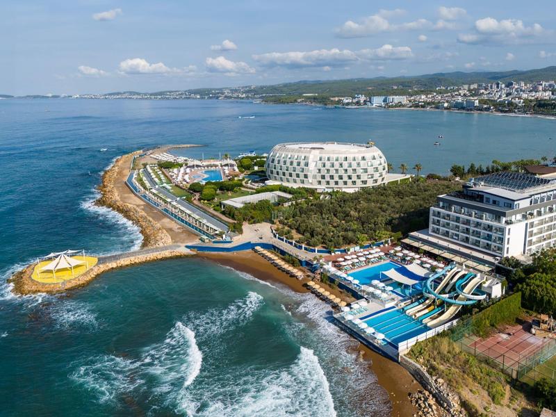 Přímořské letovisko s bazénem, moderními budovami a přímým přístupem k moři za jasného počasí.