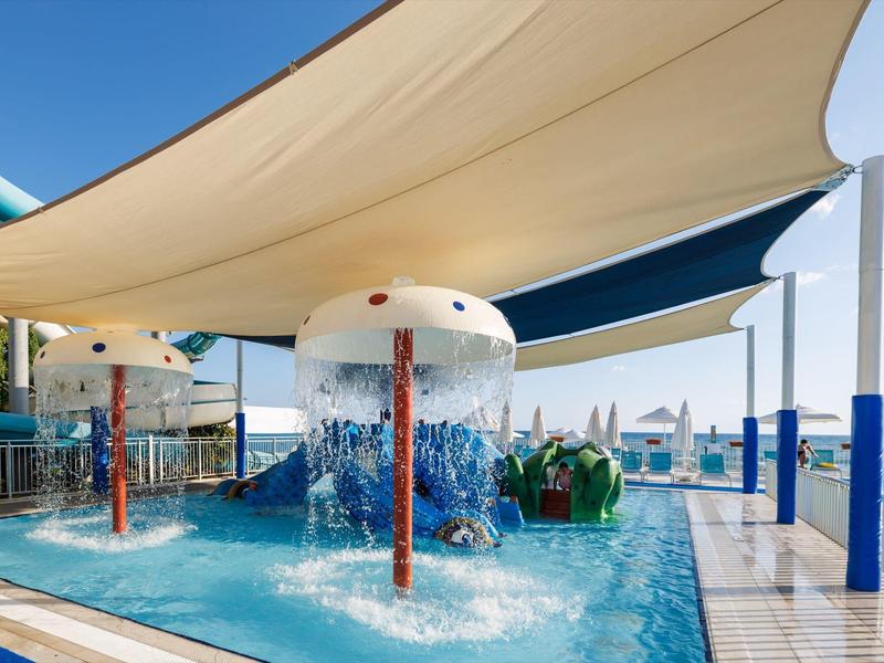 Dětský vodní park s fontánami a stínícími plachtami vedle bazénu