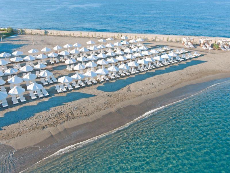 Pláž s řadami bílých slunečníků a lehátek u tyrkysového moře.