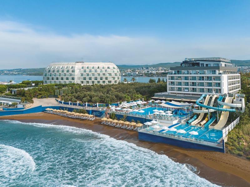 Moderní hotel s venkovním bazénem, vodními skluzavkami a výhledem na moře za slunečného dne.