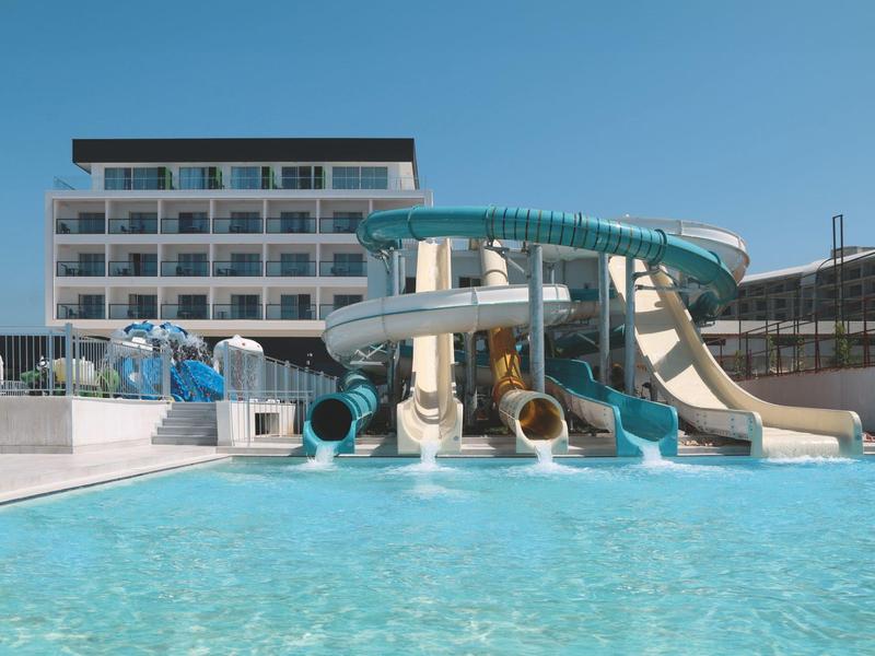 Hotelový bazén s několika vodními skluzavkami před bílou čtyřpatrovou budovou