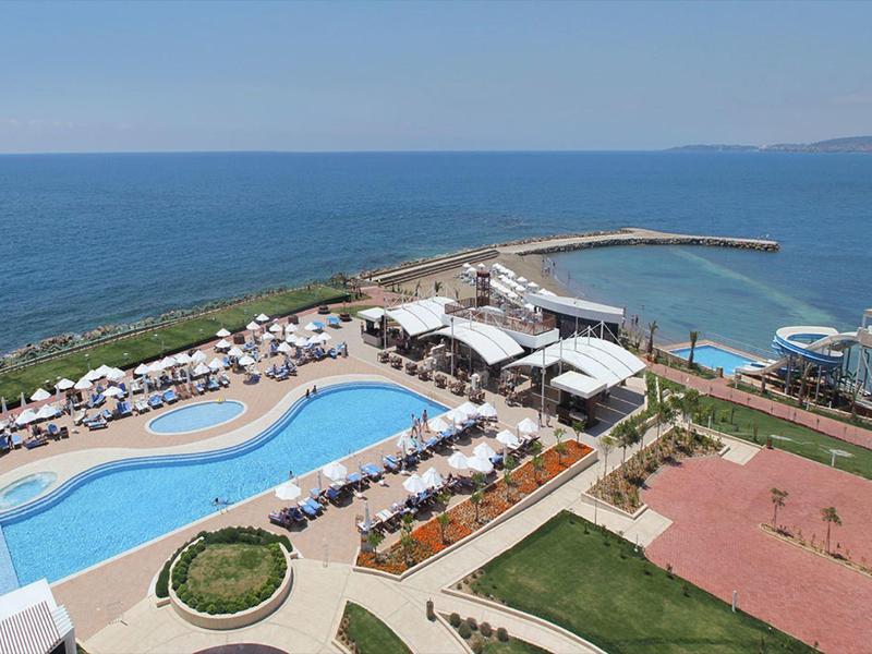 Hotelový komplex s velkým zakřiveným bazénem, lehátky a výhledem na moře