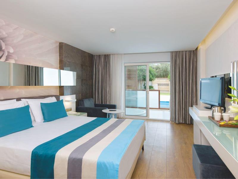 Moderní hotelový pokoj s velkou postelí, modrými akcenty a balkonem s výhledem ven.