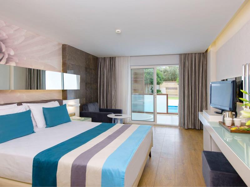 Moderní hotelový pokoj s manželskou postelí, balkónem a výhledem na bazén.