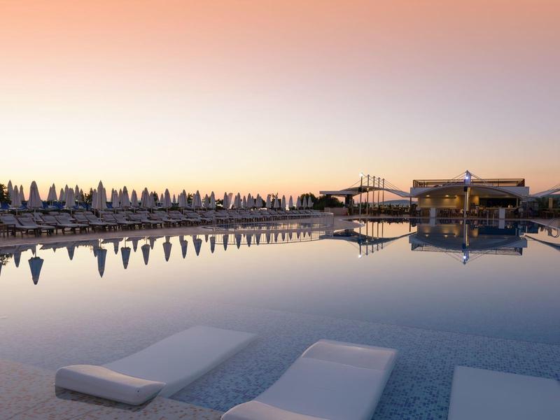 Večerní snímek klidného bazénu s lehátky a odrazy okolí