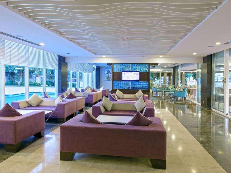 Moderní hotelová lobby s fialovými pohovkami, velkými okny a světlou mramorovou podlahou.