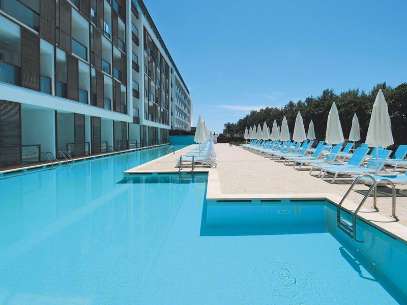 Moderní hotelový bazén s lehátky a slunečníky vedle vody pod jasnou oblohou